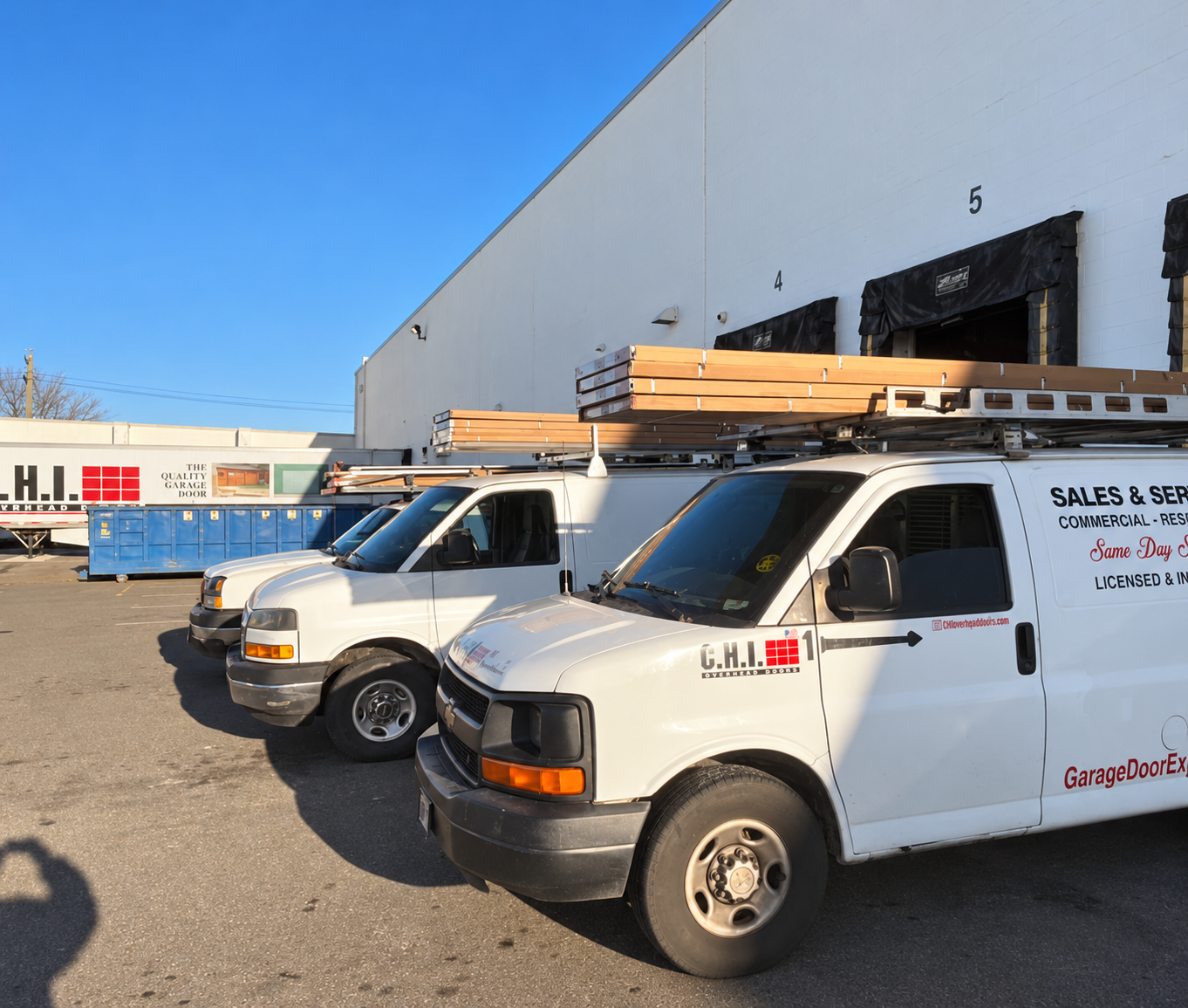 Service vans carrying garage door sections outside a warehouse
